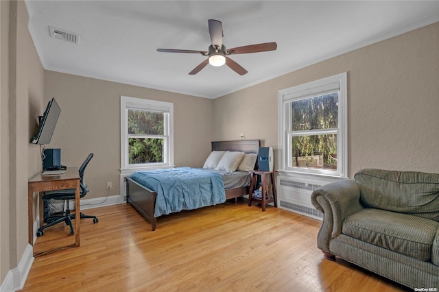 bedroom with ceiling fan, radiator heating unit, crown molding, and light wood-type flooring