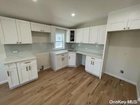 kitchen featuring white cabinetry, sink, vaulted ceiling, and light wood-type flooring