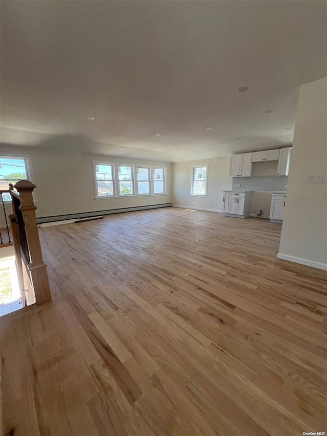 unfurnished living room with light wood-type flooring, a wealth of natural light, and a baseboard heating unit