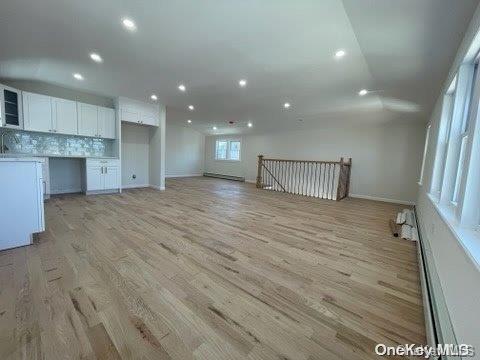 interior space featuring white cabinets, backsplash, light hardwood / wood-style floors, and a baseboard heating unit