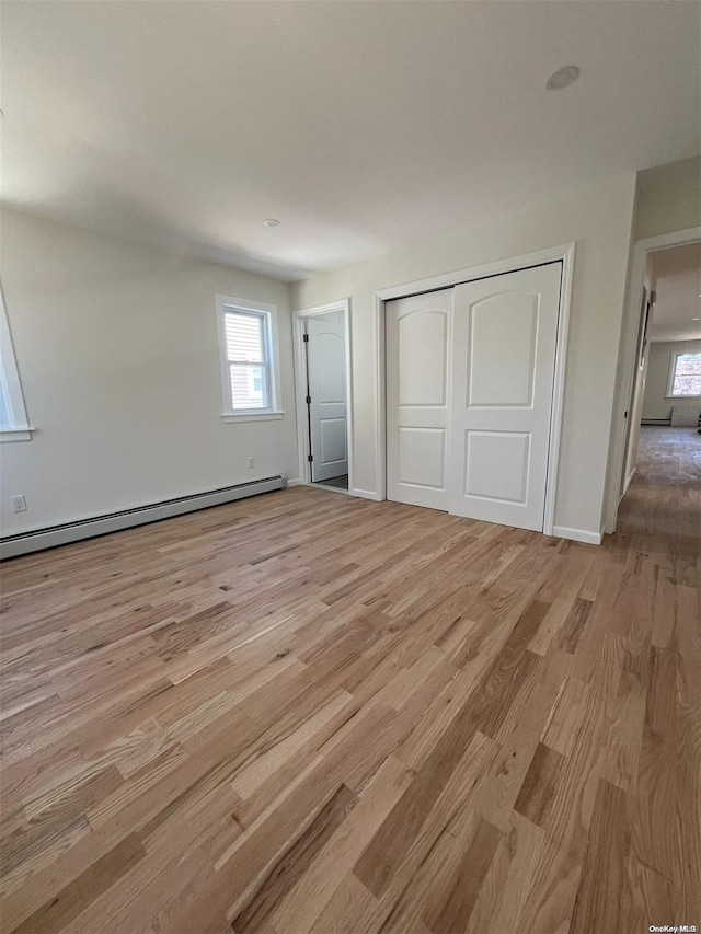 unfurnished bedroom with a closet, light hardwood / wood-style floors, and a baseboard heating unit