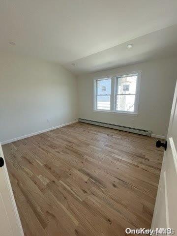 unfurnished room featuring light hardwood / wood-style flooring, lofted ceiling, and a baseboard heating unit