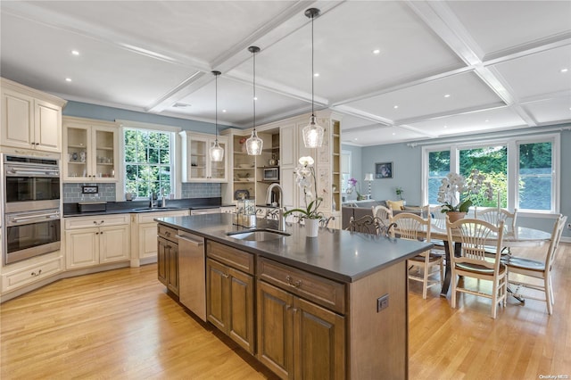 kitchen with a center island with sink, hanging light fixtures, sink, appliances with stainless steel finishes, and tasteful backsplash