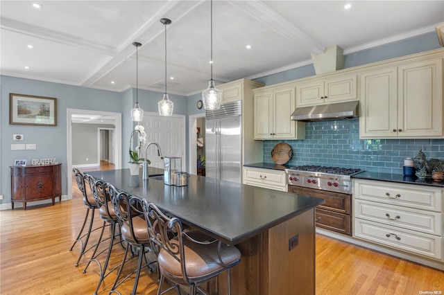 kitchen with a center island with sink, stainless steel appliances, hanging light fixtures, and cream cabinets