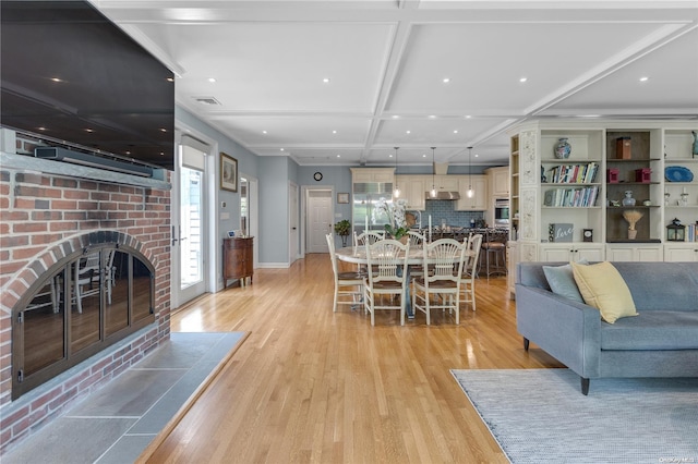 living room featuring beamed ceiling, light hardwood / wood-style floors, a fireplace, and coffered ceiling