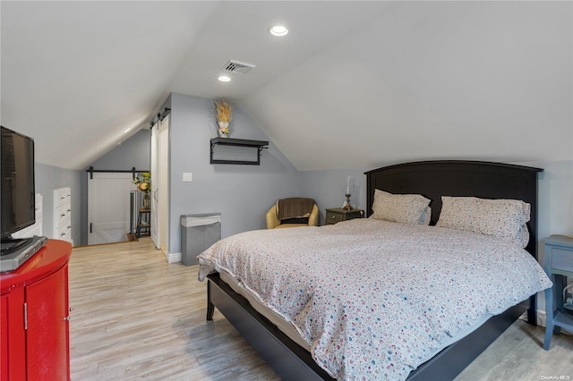 bedroom with lofted ceiling, a barn door, and light wood-type flooring