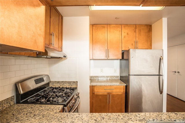 kitchen featuring hardwood / wood-style flooring, backsplash, light stone countertops, and stainless steel appliances