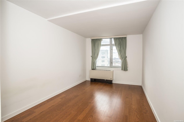 empty room with radiator heating unit and dark wood-type flooring