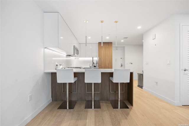 kitchen featuring white cabinets, a kitchen breakfast bar, light hardwood / wood-style floors, and hanging light fixtures