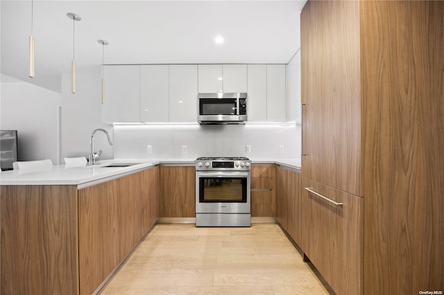 kitchen featuring appliances with stainless steel finishes, light wood-type flooring, sink, white cabinetry, and hanging light fixtures