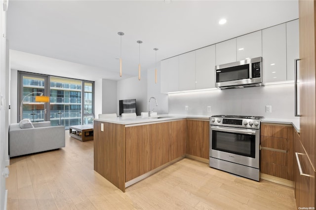 kitchen with white cabinetry, sink, kitchen peninsula, light hardwood / wood-style floors, and appliances with stainless steel finishes