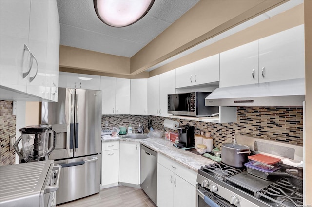 kitchen with decorative backsplash, appliances with stainless steel finishes, light wood-type flooring, sink, and white cabinetry