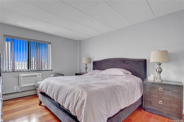 bedroom featuring an AC wall unit, a baseboard heating unit, and light hardwood / wood-style flooring