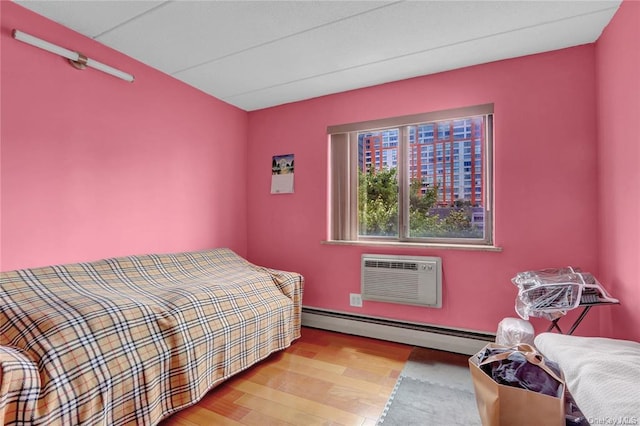 bedroom featuring a baseboard heating unit, a wall mounted air conditioner, and light hardwood / wood-style flooring