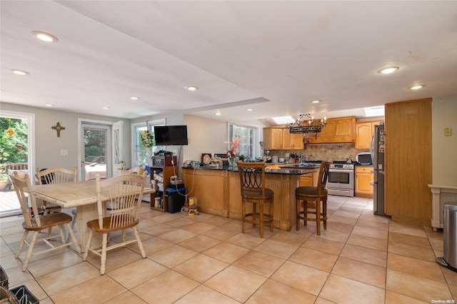 kitchen with kitchen peninsula, a breakfast bar area, decorative backsplash, light tile patterned flooring, and appliances with stainless steel finishes