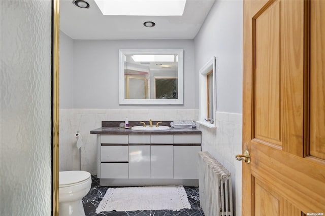 bathroom featuring radiator, a skylight, tile patterned flooring, vanity, and tile walls