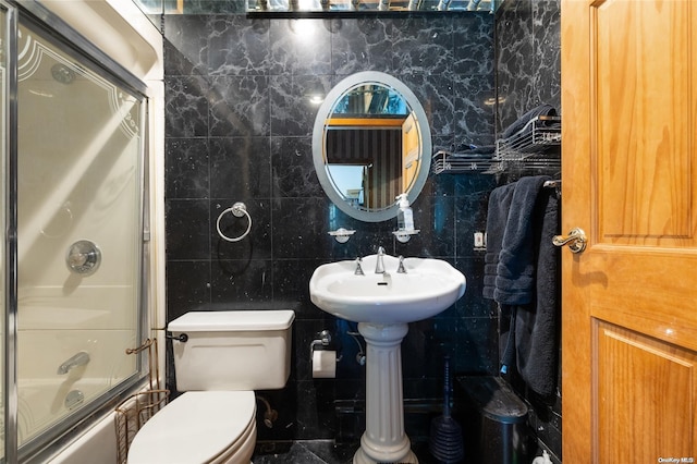 full bathroom featuring combined bath / shower with glass door, toilet, tile walls, and sink