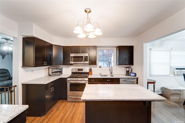 kitchen with dark brown cabinets, stainless steel appliances, sink, decorative light fixtures, and light hardwood / wood-style flooring