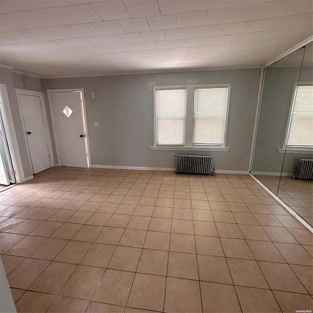 foyer entrance with radiator heating unit, ornamental molding, and light tile patterned flooring