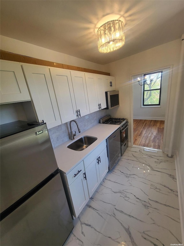 kitchen featuring sink, stainless steel appliances, an inviting chandelier, decorative backsplash, and white cabinets