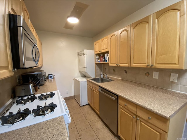 kitchen featuring sink, stacked washing maching and dryer, stainless steel appliances, backsplash, and light brown cabinetry