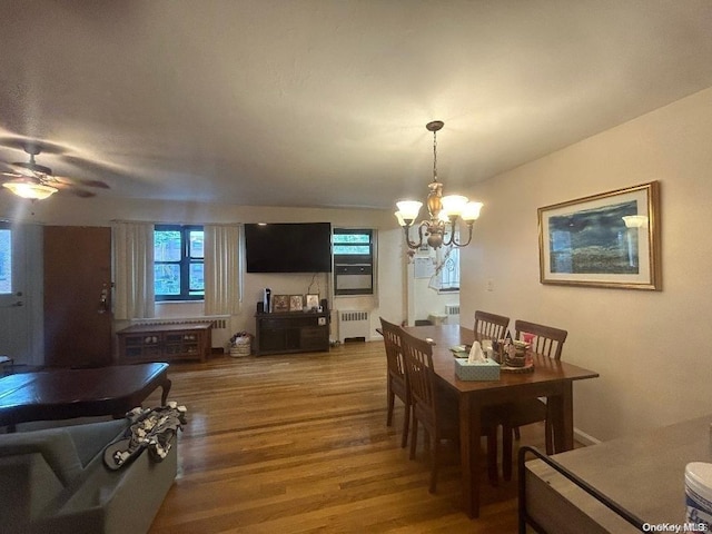 dining space with radiator heating unit, ceiling fan with notable chandelier, and hardwood / wood-style floors