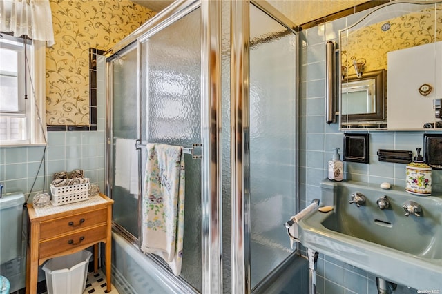 bathroom with sink, bath / shower combo with glass door, and tile walls