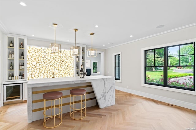 kitchen featuring crown molding, pendant lighting, a kitchen island with sink, a breakfast bar, and light parquet flooring