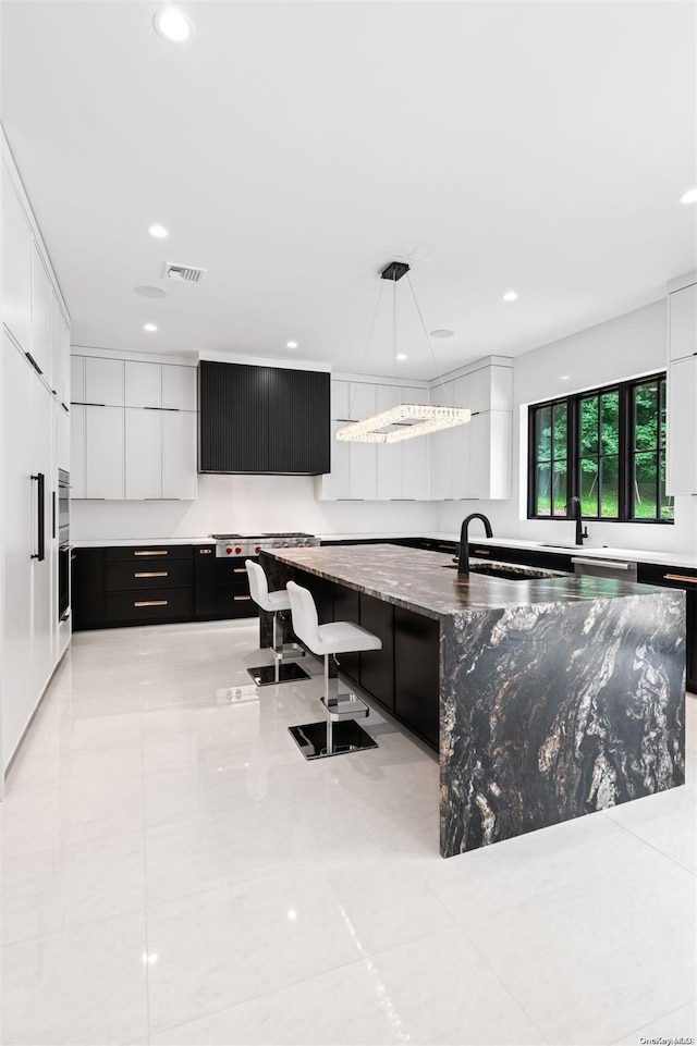 kitchen with pendant lighting, a large island with sink, white cabinets, dark stone countertops, and a kitchen bar