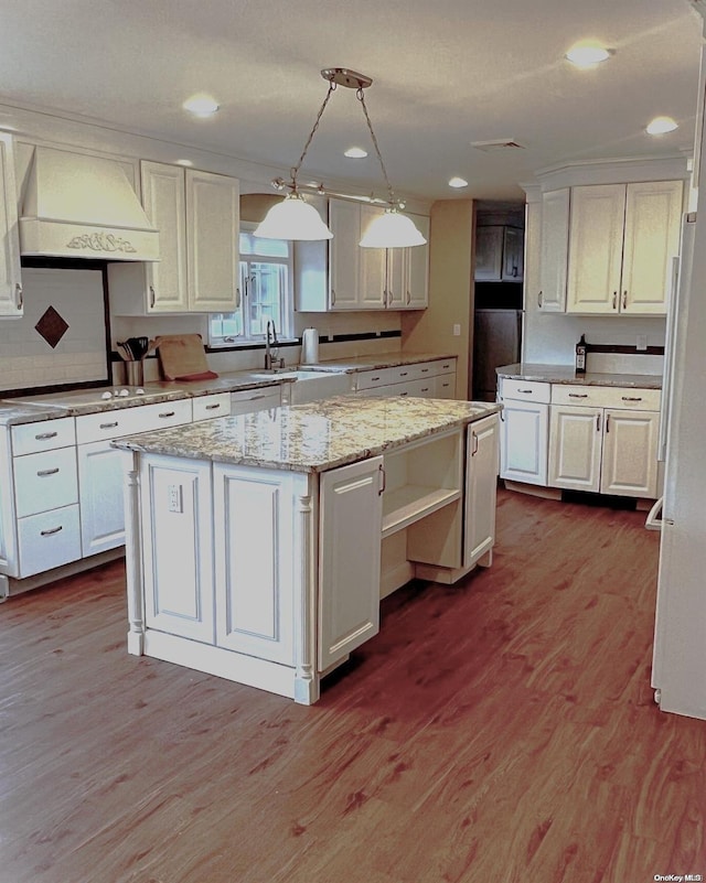 kitchen featuring white cabinets, a kitchen island, hanging light fixtures, and custom range hood