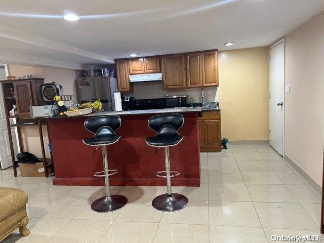 kitchen with refrigerator, light tile patterned floors, and a breakfast bar area