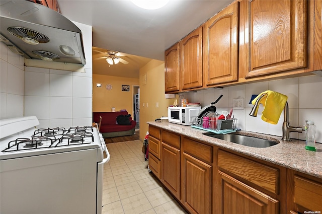 kitchen with white appliances, exhaust hood, sink, ceiling fan, and light stone countertops