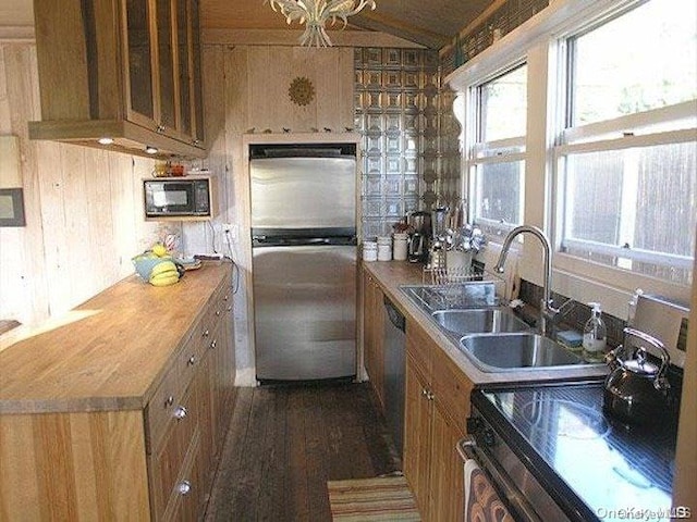 kitchen featuring sink, stainless steel appliances, an inviting chandelier, dark hardwood / wood-style flooring, and wood walls