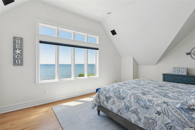 bedroom with vaulted ceiling, a water view, and light hardwood / wood-style flooring