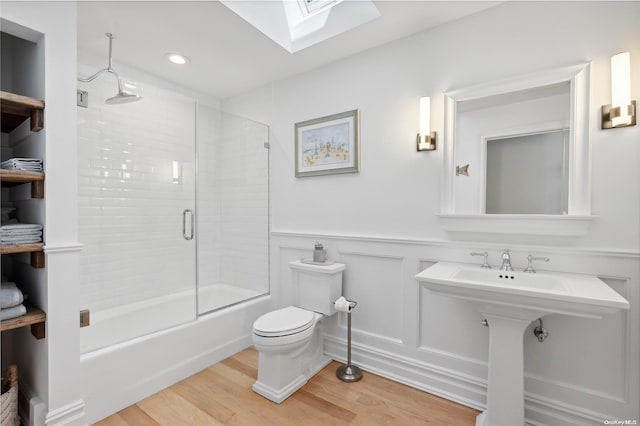 bathroom featuring wood-type flooring, a skylight, toilet, and enclosed tub / shower combo