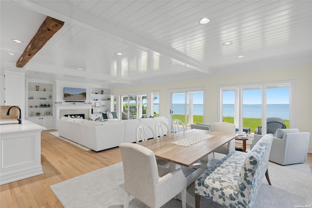 dining space featuring beamed ceiling, light wood-type flooring, and sink