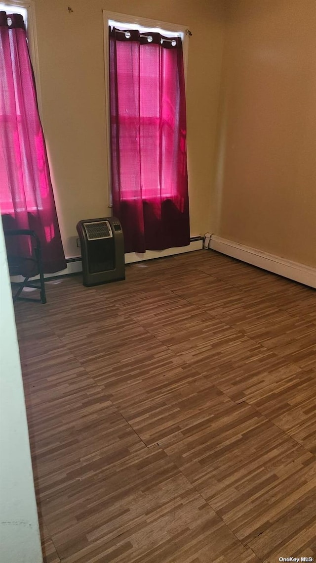 unfurnished room featuring baseboard heating and dark hardwood / wood-style flooring