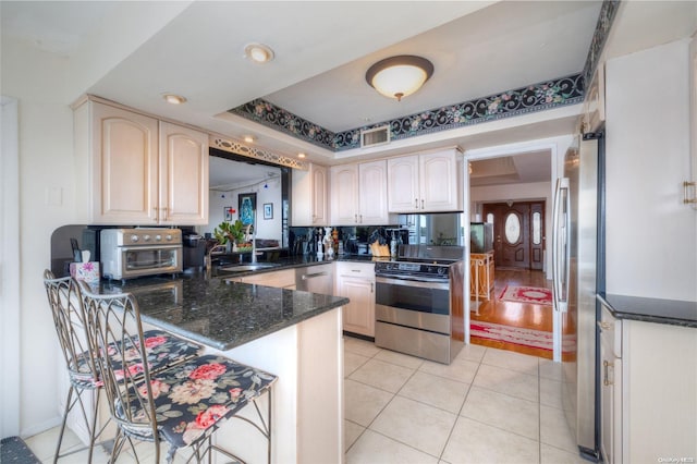 kitchen with sink, stainless steel appliances, a raised ceiling, kitchen peninsula, and light wood-type flooring