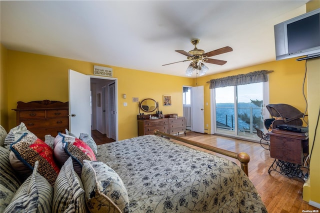 bedroom featuring hardwood / wood-style floors, ceiling fan, a water view, and access to outside