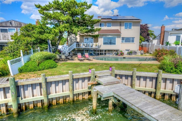 back of house featuring solar panels, a fenced in pool, a water view, a yard, and a patio area