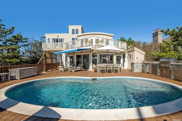 rear view of property with a swimming pool side deck, a balcony, and exterior kitchen