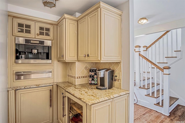 kitchen with light stone countertops, beverage cooler, cream cabinetry, decorative backsplash, and light wood-type flooring