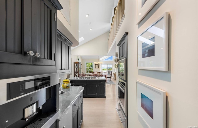 kitchen featuring stainless steel appliances, a towering ceiling, a chandelier, stone countertops, and light hardwood / wood-style floors