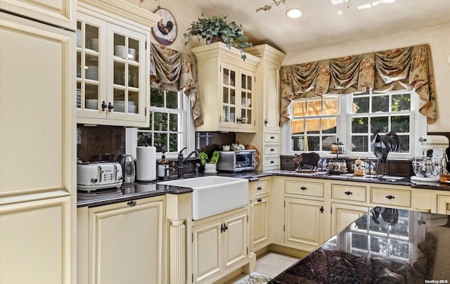 kitchen featuring sink, light tile patterned flooring, dark stone counters, and cream cabinetry