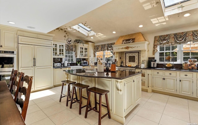 kitchen with vaulted ceiling with skylight, paneled fridge, stainless steel double oven, cream cabinets, and a center island