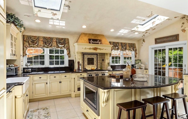 kitchen featuring a breakfast bar, a center island, stainless steel microwave, lofted ceiling with skylight, and cream cabinets