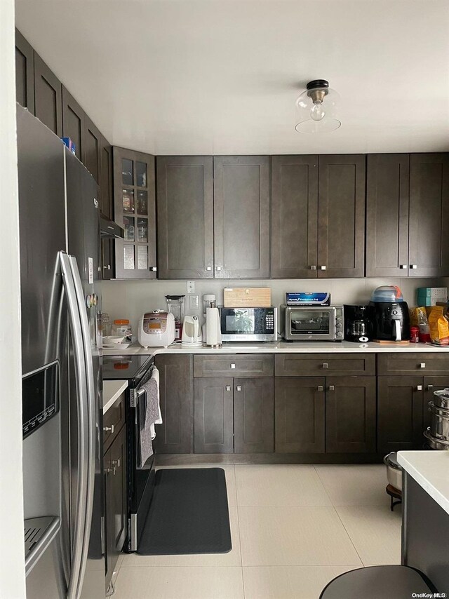 kitchen with dark brown cabinets, light tile patterned floors, and appliances with stainless steel finishes