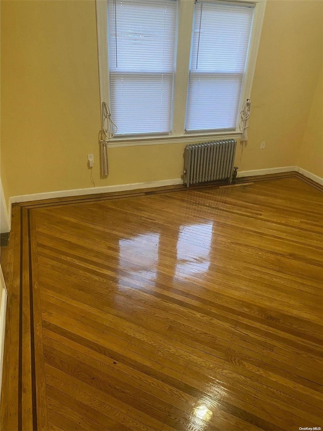 unfurnished room featuring wood-type flooring, radiator heating unit, and a wealth of natural light