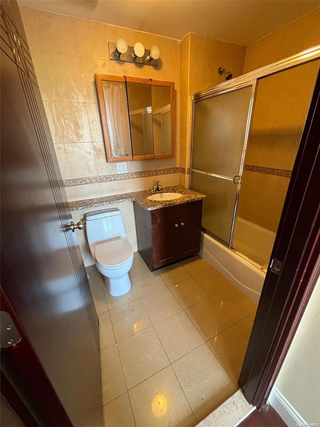 full bathroom featuring tile patterned floors, bath / shower combo with glass door, toilet, vanity, and tile walls