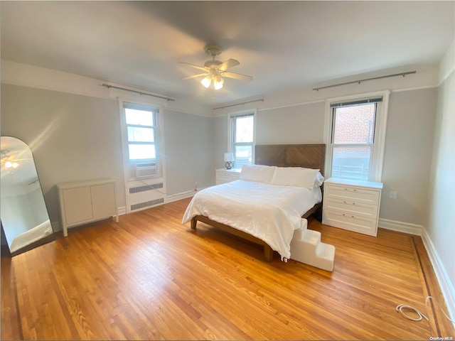 bedroom featuring radiator, light hardwood / wood-style floors, ceiling fan, and cooling unit